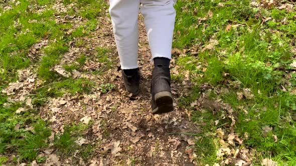 Low angle track shot of female person walking on forest path with falling leaves and green grass fie