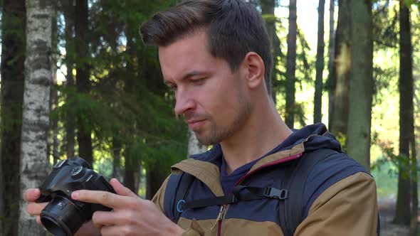 A Young Handsome Hiker Takes Pictures with a Camera in a Forest - Closeup