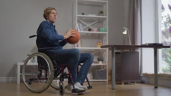 Young Sportsman in Wheelchair Throwing Basketball Ball in Slow Motion Training at Home Indoors