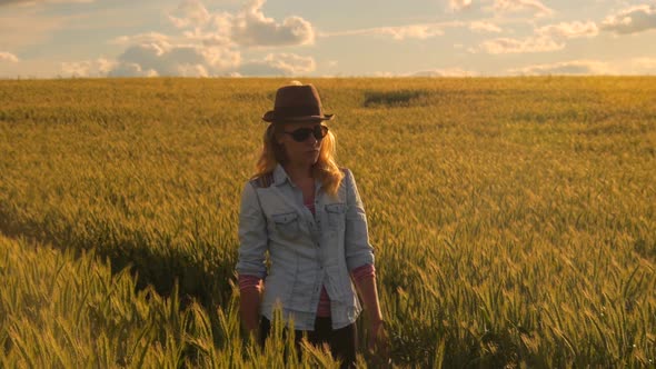 young caucasian bohemian female wearing hat in a  barley field during sunset