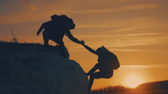 Silhouette of Helping Hand Between Two Climber. Two Hikers on Top of the Mountain, a Man Helps a