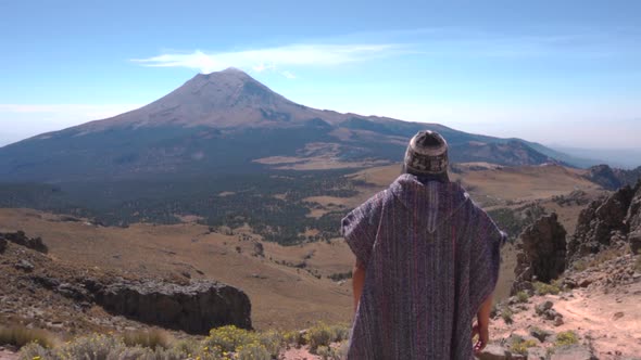 Back view of man trekker standing and looking at steaming active Popocatepetl volcano