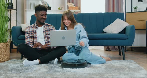 Multiethnic Couple which Watching Interesting Video on Laptop on the floor