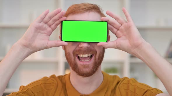 Portrait of Joyful Redhead Man Having Smartphone with Chroma Screen Over Eyes 