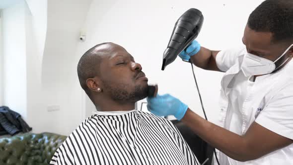 Barber blow-drying and brushing beard of customer