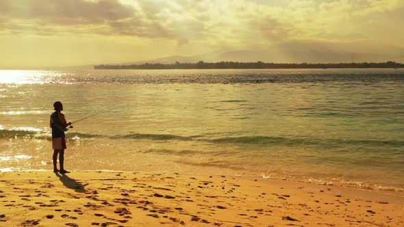 Man alone fishing alone on exotic coastline beach holiday by clear ocean with white sand background 