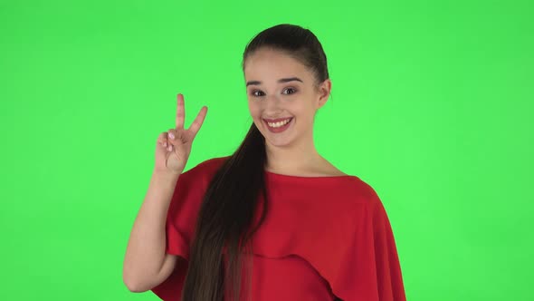 Portrait of Pretty Young Woman Is Showing Two Fingers Victory Gesture. Green Screen