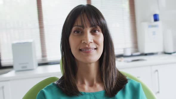 Portrait of smiling biracial female patient sitting on chair at modern dental clinic