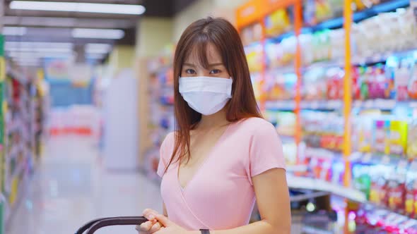 Asian beautiful woman wearing face mask and holding shopping basket in supermarket department store.