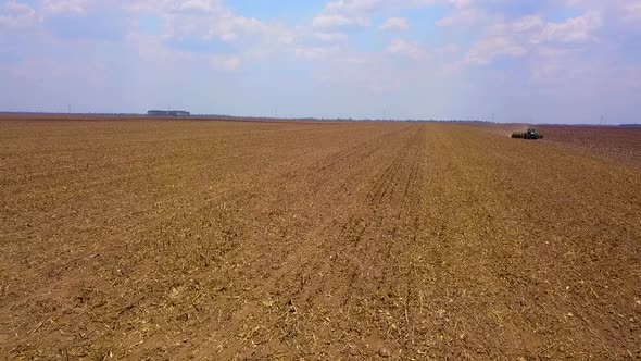 Slow aerial drone shot flying towards a tractor plowing a dry field