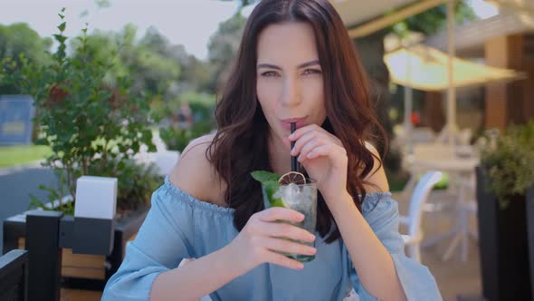 Beauiful Woman Sitting in Outdoor Restaurant and Sip Mojito Dring in Summer Hot Day