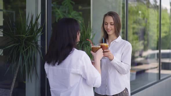 Positive Young Women Standing on City Street Drinking Cocktails in Slow Motion Smiling