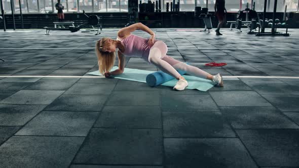 A flexible girl athlete rolls her muscles with a roller on a karemat in the gym.