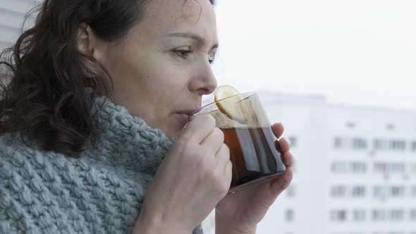 A woman in a warm scarf drinking tea by the window.