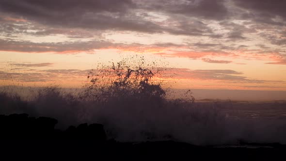 Rough Atlantic ocean waves crashing against rocky shore with orange sunset