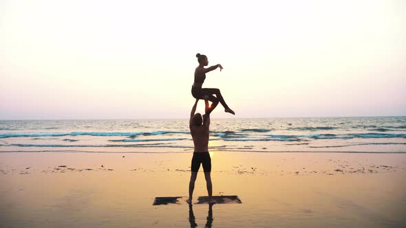 Fit Sporty Couple Practicing Acro Yoga with Partner Together on the Sandy Beach