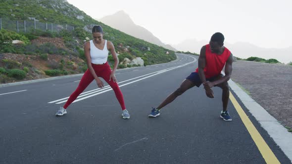 Diverse fit couple exercising stretching on a country road near mountains