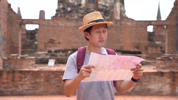 Young Asian Man with Hat Looking at Map in Traditional Temple in Ayutthaya Historic Park Thailand