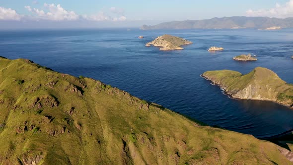 Padar island southern tip with Komodo isle in the distance in Indonesia, Aerial pan right reveal sho