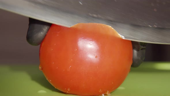 The chef cuts a ripe tomato with a large knife, close-up