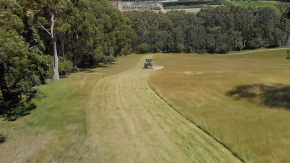 Aerial shot following a tractor slashing dry grass down a hill in rural Australia.