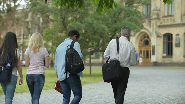 Multiracial students walking with their dean to academy, chatting about thesis