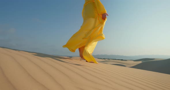 Model in Yellow Fashion Dress Walking Barefoot By Wavy Sand Surface in Desert