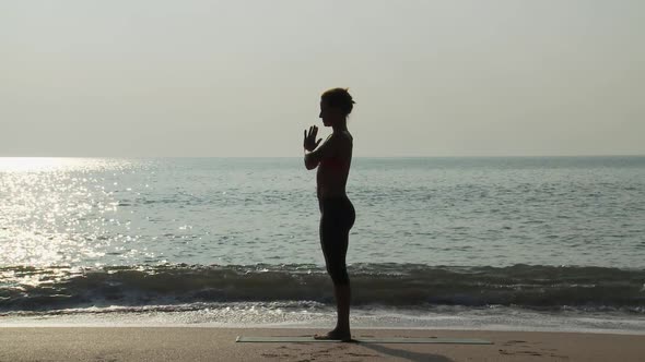 Silhouette of woman by sea in prayer pose