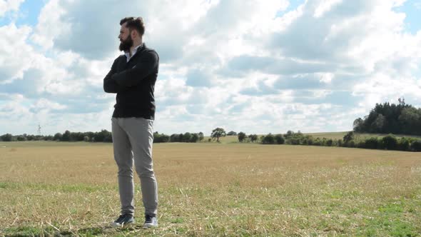 Young Handsome Hipster Man Stands in Field and Looks Around - Cloudy Sky