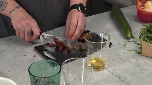 Oily sundried tomato is cut up on small kitchen counter cutting board