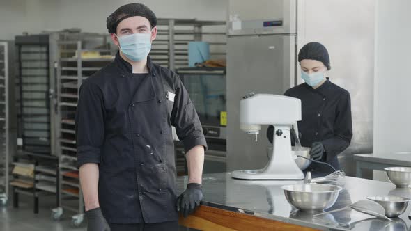 Confident Man in Coronavirus Face Mask and Cook Uniform Turning Looking at Camera with Blurred