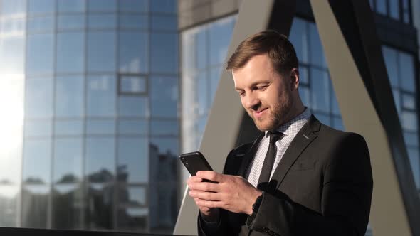 Happy Businessman Holding a Smartphone and Laughing