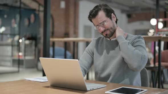 Young Man Having Neck Pain While Using Laptop in Office