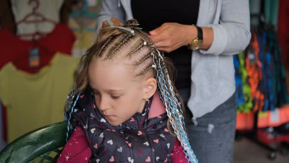 Female Hairdresser Braiding Hair of Little Girl