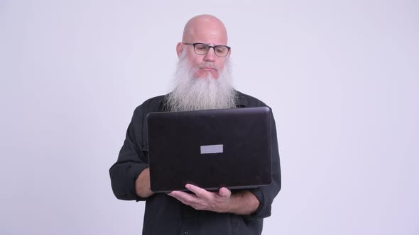 Happy Mature Bald Bearded Man Thinking While Using Laptop