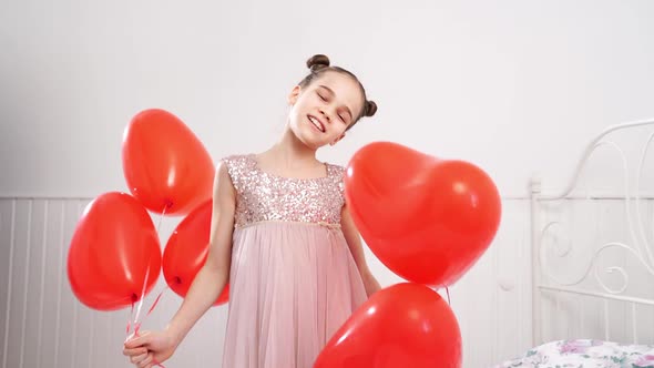 Teen Girl Dances Laughs with Red Balls of Hearts on the Bed Near White Wall