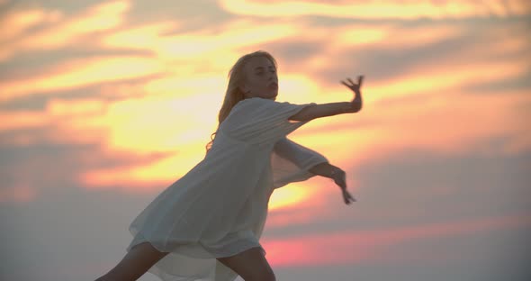 Beautiful Young Woman in White Dress is Dancing During Colorful Sunset