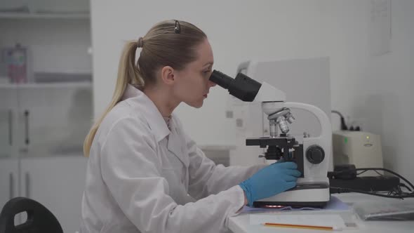 Female Medical Professional Works with Samples and Analyzes in Medical Laboratory Behind Microscope