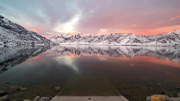 Time lapse of sunrise reflecting over lake surrounded by snow capped mountains