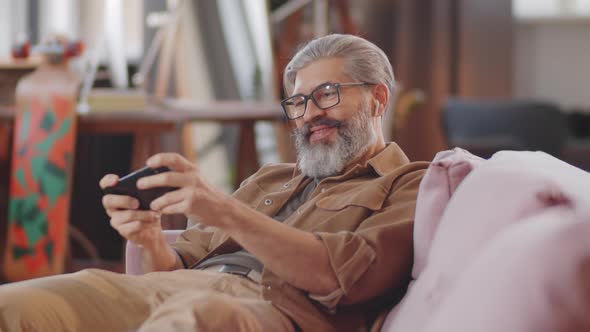 Happy Mid Age Man Playing Game on Smartphone at Home