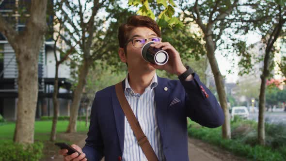 Asian man holding coffee cup using smartphone while walking in the park