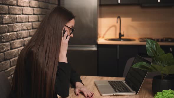 Confident Freelancer Pretty Caucasian Woman in Glasses Talking on Phone Using Laptop at Home or