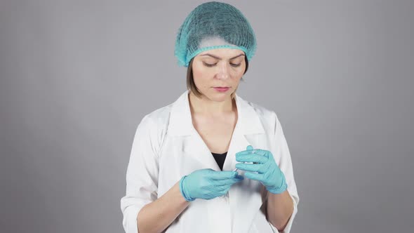 Young Female Doctor in Gloves Holding a Syringe and Preparing Injection Isolated on Grey Background