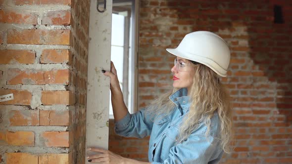 A Female Architect or Bricklayer Stands in a Newly Built House with Untreated Walls and Checks the