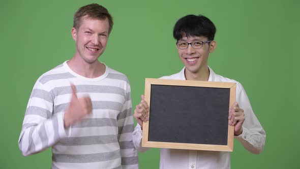 Two Happy Young Multi-ethnic Businessmen Showing Blackboard and Giving Thumbs Up