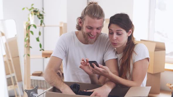 Smiling Caucasian Pair Looking at Smartphone in New Apartment in Slowmotion