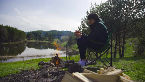 Man by campfire against lake view.