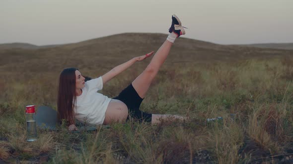 Pregnant Caucasian Woman is Lying on Lawn and Doing Yoga Stretching Her Leg