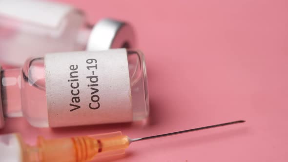 Close Up of Coronavirus Vaccine and Syringe on Pink Background