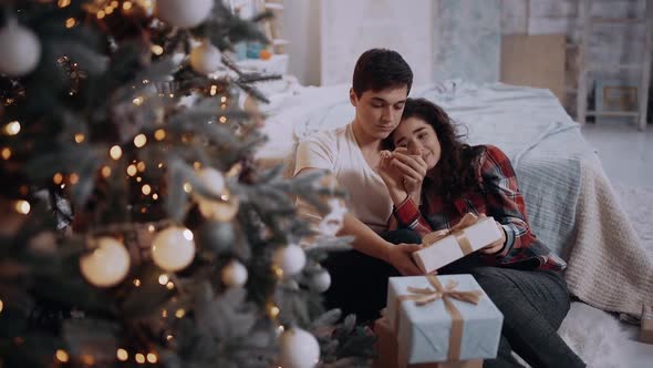 Loving Couple Dressed in Winter Sweaters Spend Romantic Time Sitting Next To the Christmas Tree.